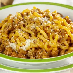 Piatto di gramigna alla salsiccia, condita con ragù e parmigiano grattugiato, servita in una ciotola bianca con bordo verde.