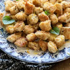 Croccante spezzatino di pollo impanato, guarnito con scorza di limone e menta fresca, servito su un piatto decorato.