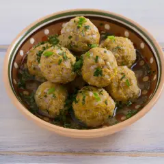 Polpette di riso avanzato, dorate e profumate, servite in una ciotola decorata, con erbe fresche tritate.
