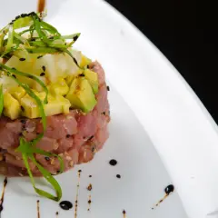 Deliziosa tartare di tonno con avocado, ananas e cipollotto fresco, guarnita con semi di sesamo e un filo di salsa.