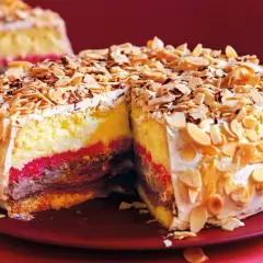 Una fetta di pizza dolce abruzzese, con strati di crema, cioccolato e confettura, ricoperta di mandorle tostate e scaglie di cioccolato.