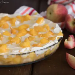Delizioso tiramisù alle pesche in una pirofila di vetro, guarnito con pesche a pezzetti e panna montata.