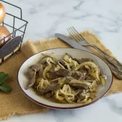 Piatto di fegato alla veneziana con cipolle dorate, accompagnato da cipolle fresche in un cestino e foglie di salvia.