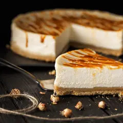 Una fetta di cheesecake senza gelatina, con caramello colante, su un tavolo di legno scuro.
