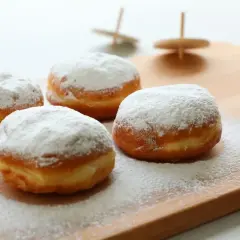 Quattro soffici bomboloni alla crema, cosparsi di zucchero a velo, invitano a un dolce momento.