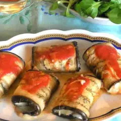 Deliziosi involtini di melanzane ripieni, conditi con sugo di pomodoro, su un piatto decorato.