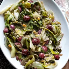 Scarola in padella con olive nere e pinoli, un contorno saporito e colorato, pronto per essere gustato.