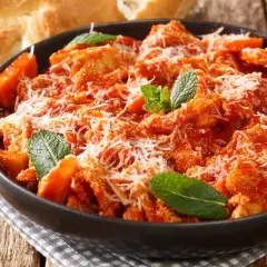 Trippa alla romana, la ricetta della nonna, servita in una ciotola scura con parmigiano e menta. Accanto, pane casereccio.