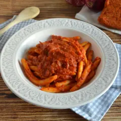 Piatto di pasta con sugo rosso piccante, condita con nduja calabrese. Accanto, un pezzo di nduja e cipolla rossa.