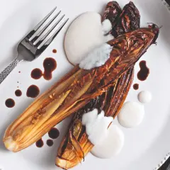 Radicchio al forno caramellato, servito con crema bianca e salsa scura su un piatto bianco, con forchetta e coltello.