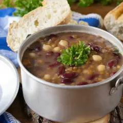 Una fumante zuppa di legumi, ricca di fagioli rossi, lenticchie e ceci, guarnita con prezzemolo fresco, accanto a pane casereccio.