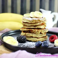 Pancakes alla banana soffici e dorati, guarniti con fettine di banana, frutti di bosco e zucchero a velo.