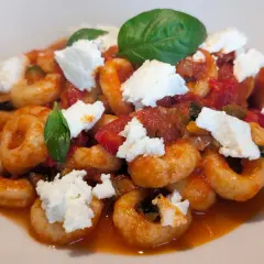 Anellini alla pecorara con pomodoro, zucchine e ricotta fresca, guarniti con basilico. Un piatto saporito e invitante.