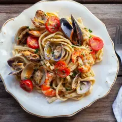 Un piatto invitante di scialatielli ai frutti di mare, con cozze, vongole e gamberi, guarnito con pomodorini e prezzemolo.