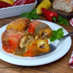 Deliziosi involtini di peperoni ripieni, dorati e succulenti, serviti su un piatto bianco con menta fresca.