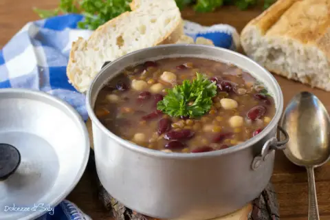 Una fumante zuppa di legumi, ricca di fagioli rossi, lenticchie e ceci, guarnita con prezzemolo fresco, accanto a pane casereccio.
