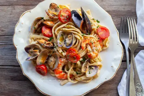 Un piatto invitante di scialatielli ai frutti di mare, con cozze, vongole e gamberi, guarnito con pomodorini e prezzemolo.