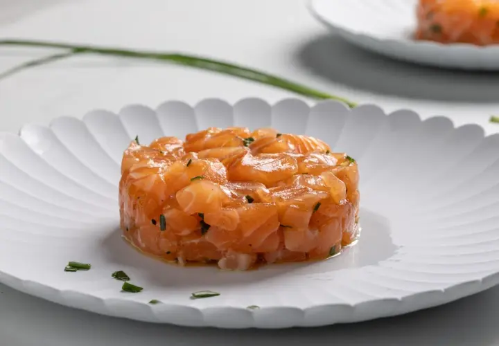 Tartare di salmone fresco, finemente tagliato e condito, servito su un piatto bianco con erba cipollina.