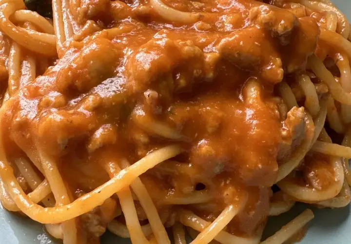 Un piatto di spaghetti al ragù, con un sugo ricco e saporito, dove spiccano i pomodorini.