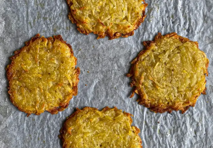 Quattro rosti di patate dorati e croccanti su carta da forno.