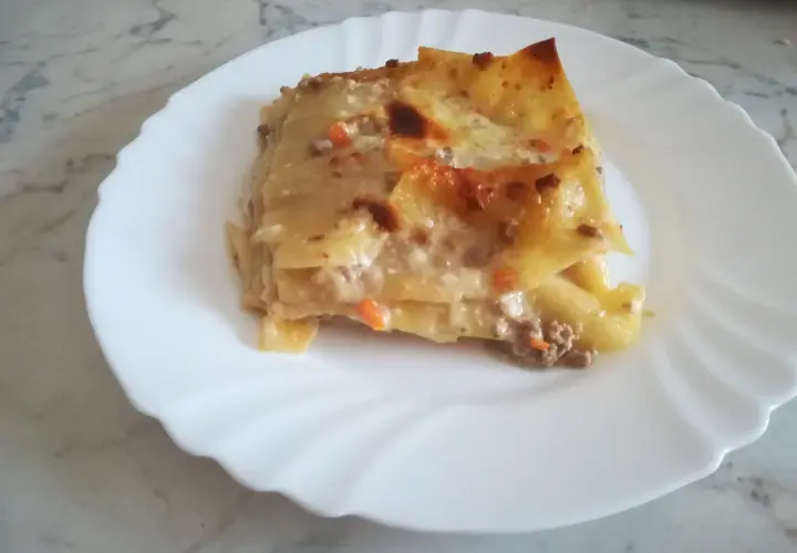 Porzione di lasagna classica, con strati di pasta, ragù e besciamella, servita su un piatto bianco.