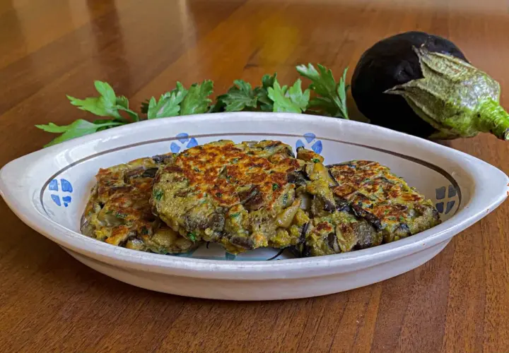 Tre hamburger di melanzane dorati e appetitosi in un piatto decorato, con un'altra melanzana e prezzemolo sullo sfondo.