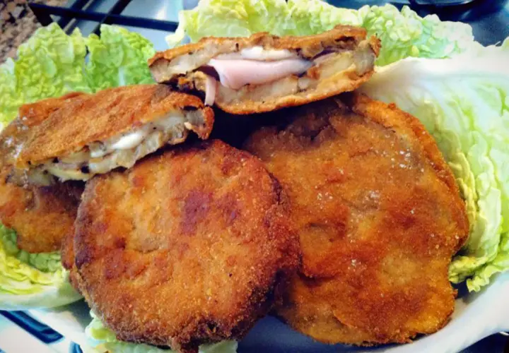 Cordon bleu di melanzane dorati e croccanti, ripieni di prosciutto e formaggio filante, serviti su un letto di lattuga fresca.