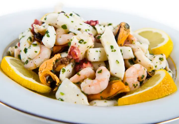 Deliziosa insalata di mare con gamberi, calamari, polpo e cozze, condita con prezzemolo e limone.