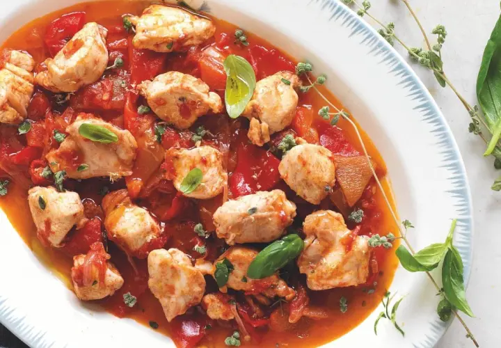 Piatto di coniglio alla cacciatora ricetta della nonna, con pezzi di carne tenera in salsa di pomodoro e peperoni, guarnito con basilico fresco e timo.