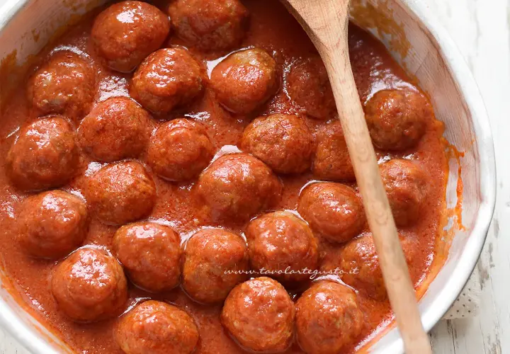 Polpette al sugo succulente in una ciotola bianca, pronte per essere gustate. Un cucchiaio di legno le accompagna.