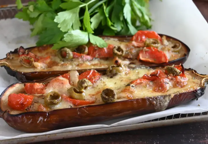 Melanzane alla pizzaiola, gustose e filanti, con pomodoro, olive e formaggio fuso, guarnite con prezzemolo fresco.