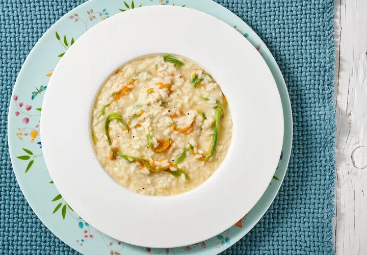 Un piatto di risotto ai fiori di zucca cremoso, con petali arancioni e fili verdi che si intrecciano nel riso bianco.