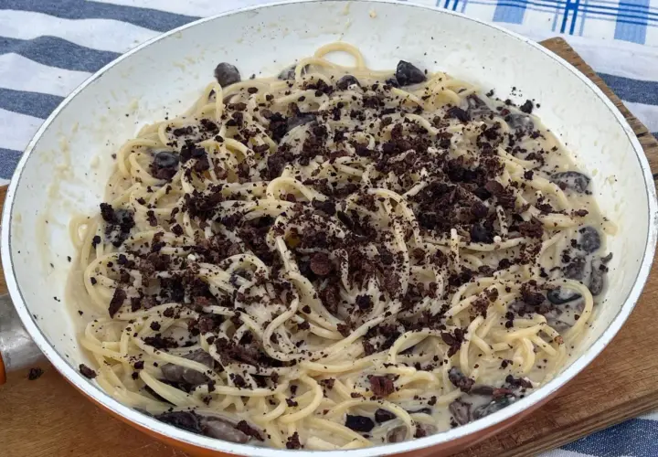 Spaghetti cremosi con olive nere e una spolverata di briciole scure, un'interpretazione audace della pasta alla cenere.