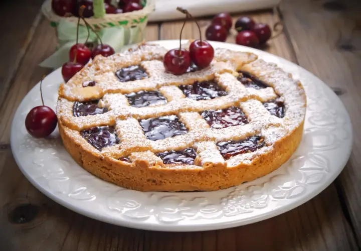 Deliziosa crostata senza burro con marmellata di ciliegie, cosparsa di zucchero a velo e decorata con ciliegie fresche.