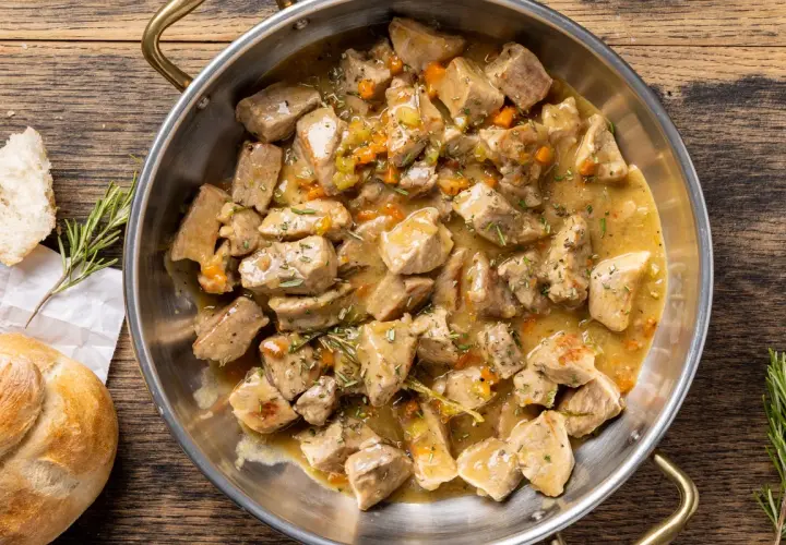 Un saporito spezzatino di vitello in umido, con carote e rosmarino, servito in una padella di metallo su un tavolo di legno.