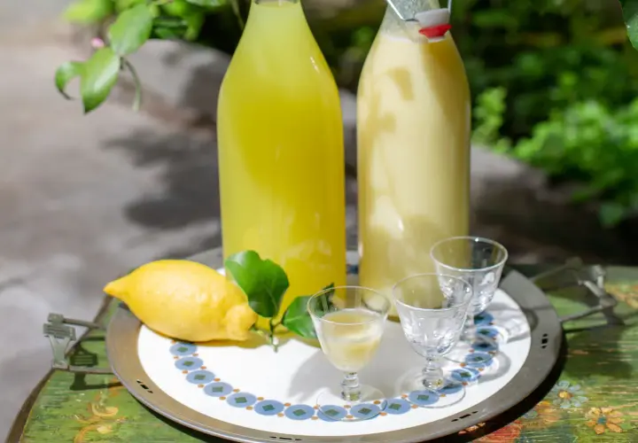 Due bottiglie di limoncello, una chiara e una cremosa, con limone fresco e bicchierini pronti per un assaggio.