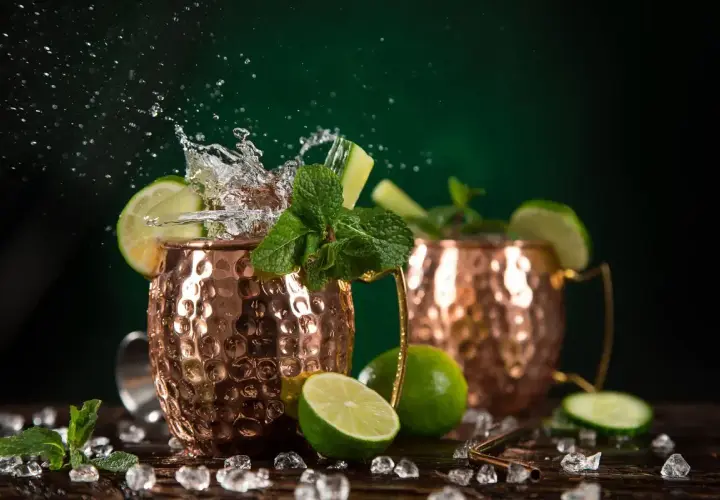 Moscow Mule ricetta: due tazze di rame con schizzi d'acqua, lime, menta e cetriolo. Fresco e dissetante.