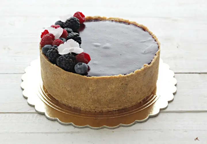 Delizioso cheesecake ai frutti di bosco con copertura al cioccolato fondente, decorato con lamponi, mirtilli e more freschi.