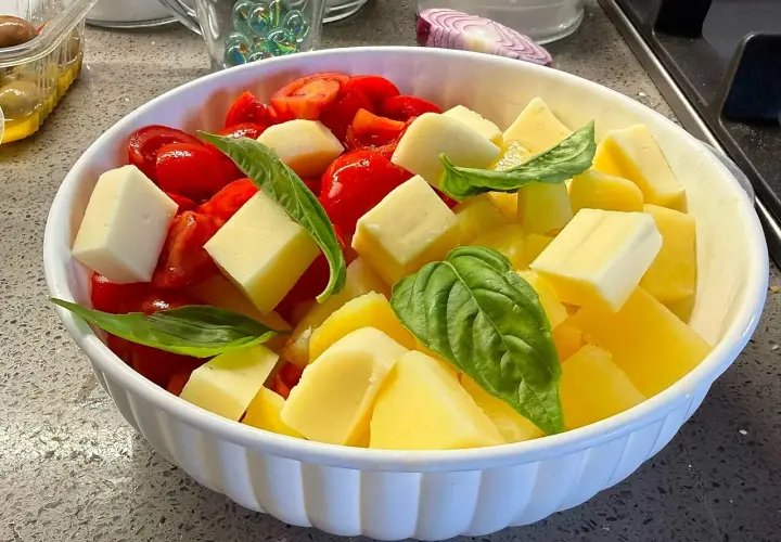 Insalata di pomodori freschi, cubetti di formaggio e foglie di basilico in una ciotola bianca.