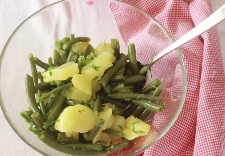 Insalata di fagiolini e patate, condita con erbe fresche, servita in una ciotola di vetro su un tovagliolo a quadretti rossi.