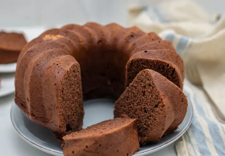 Un delizioso ciambellone al cioccolato, soffice e invitante, con una fetta tagliata che mostra la sua morbidezza.