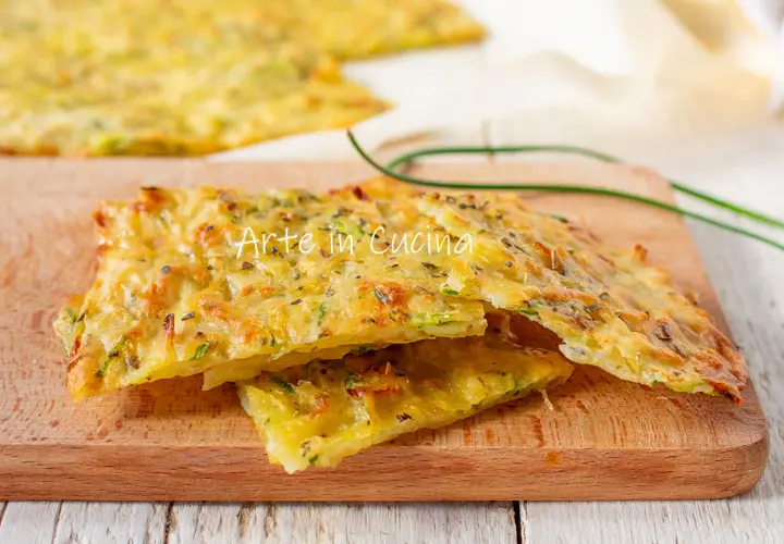 Schiacciata di zucchine dorata e croccante, condita con erbe aromatiche, servita su un tagliere di legno.