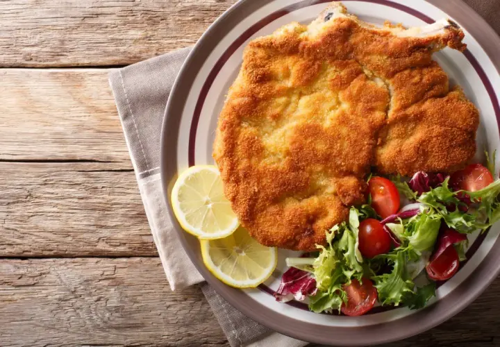 Una dorata cotoletta alla milanese, croccante e succulenta, servita con spicchi di limone e un'insalata fresca.