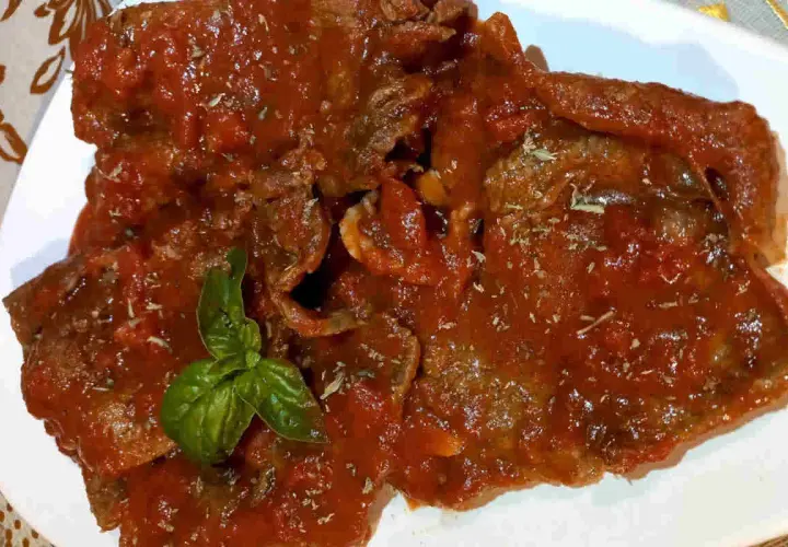 Fette di carne alla pizzaiola siciliana, ricoperte da un sugo rosso saporito e guarnite con basilico fresco.
