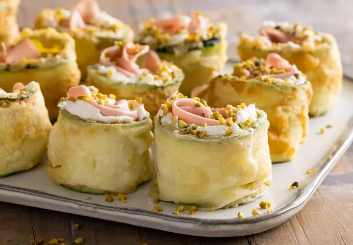 Rotolini di zucchine fritte con crema, prosciutto e pistacchi: stuzzichini veloci ed economici per aperitivo.