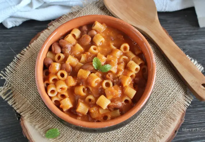 Un piatto fumante di pasta e fagioli in scatola, guarnito con menta fresca, servito in una ciotola di terracotta su una tovaglietta di juta.