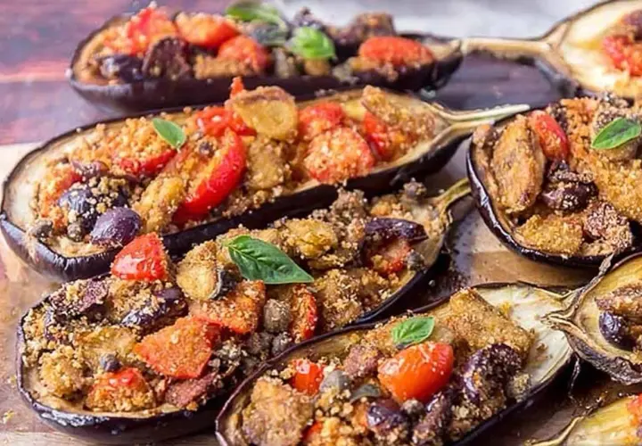 Melanzane a scarpone ripiene di pomodorini, olive e pangrattato, guarnite con basilico fresco. Un piatto saporito e invitante.