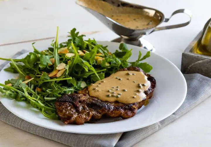 Un succulento filetto al pepe verde, nappato con la sua salsa cremosa, accompagnato da un'insalata fresca di rucola e mandorle.
