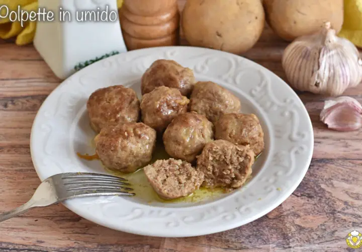 Polpette in umido succulente su un piatto bianco, con una forchetta pronta ad assaggiarle. Sullo sfondo, patate e aglio.