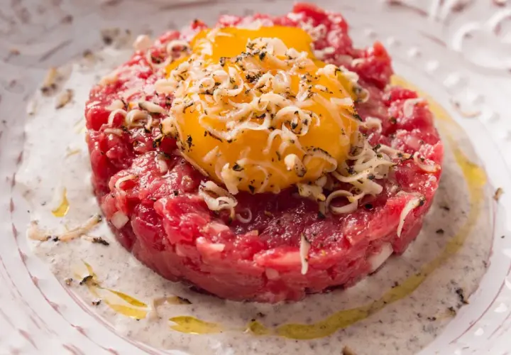 Tartare di manzo con tuorli d'uovo, cipolla e formaggio grattugiato. Un'idea su come condirla per un piatto gourmet.